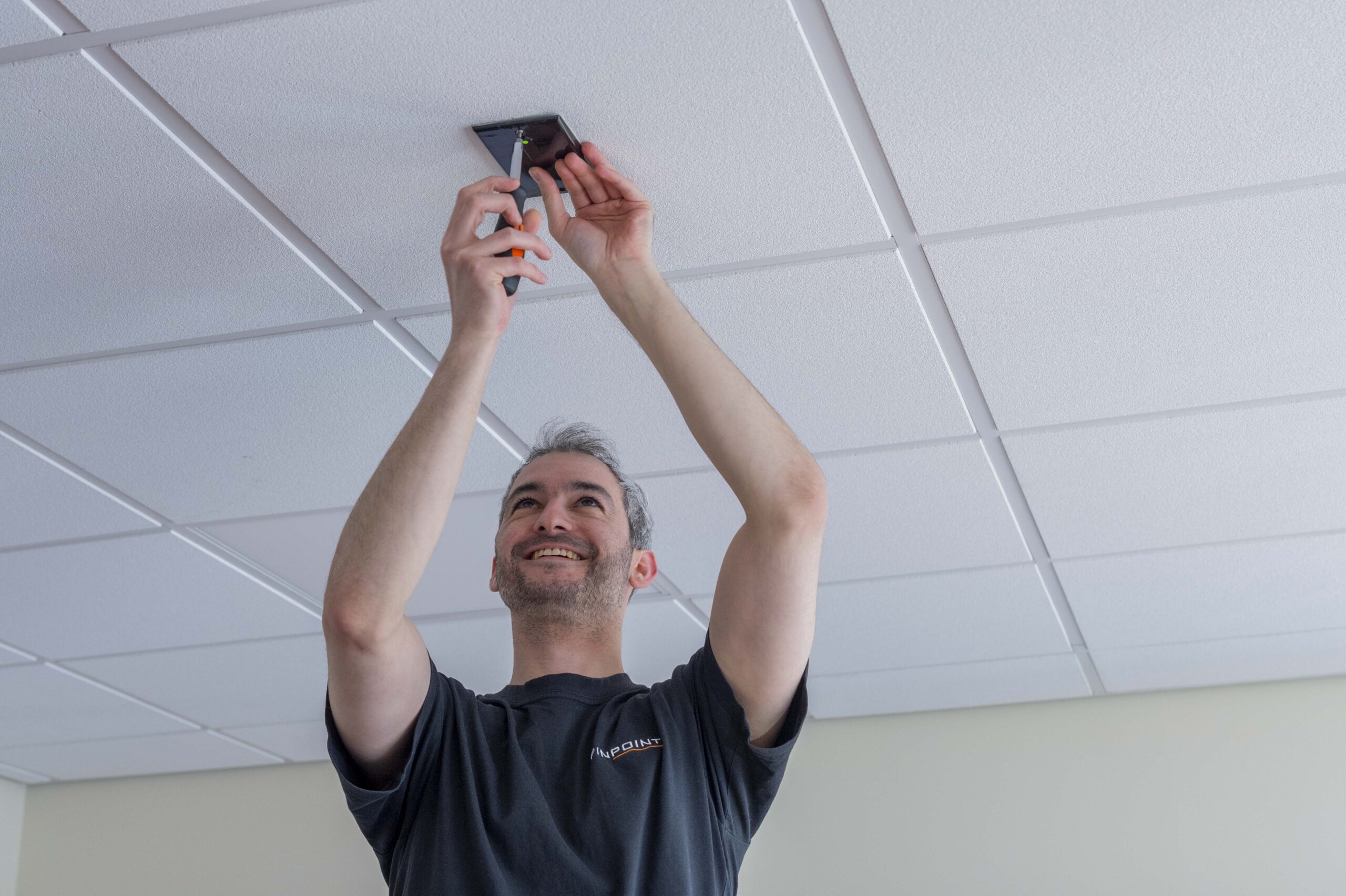 A pinpoint engineer installing a Pinpoint System to the ceiling of a room.